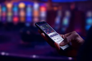 Arka planda canlı istatistiklerle dizüstü bilgisayarına odaklanan bir adam, PARA BET mobil uygulamasının spor ve oyun özelliklerini vurgular.